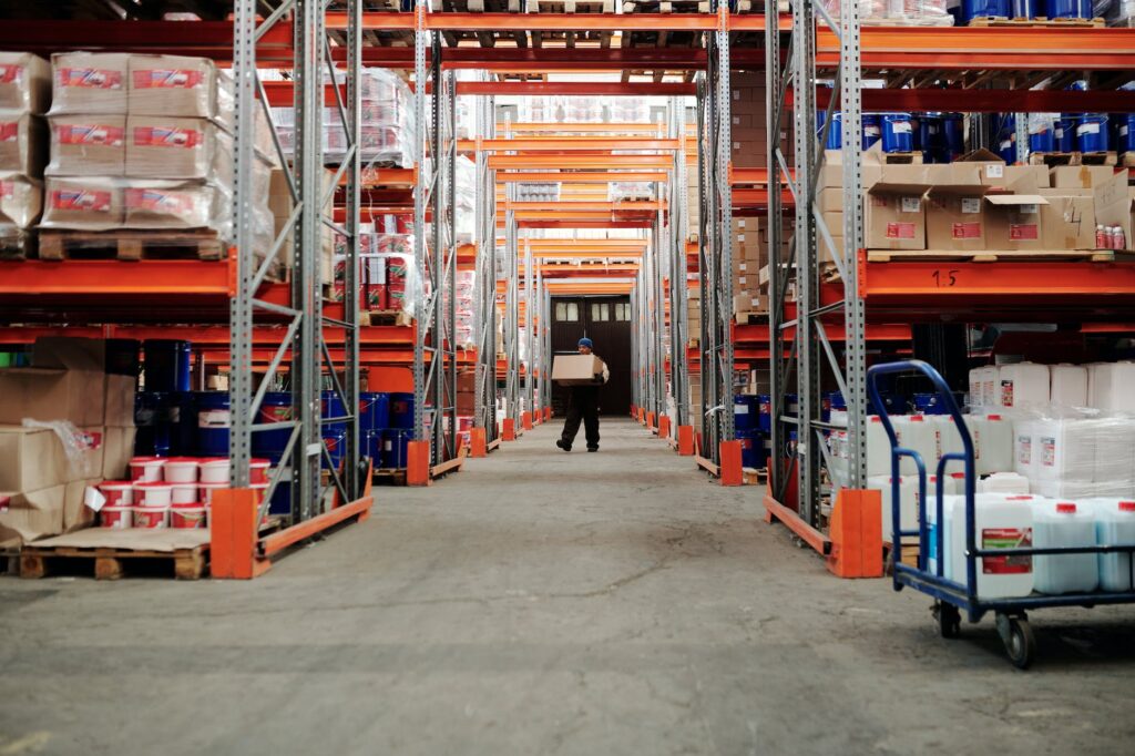 man standing in an aisle of a warehouse carrying a box